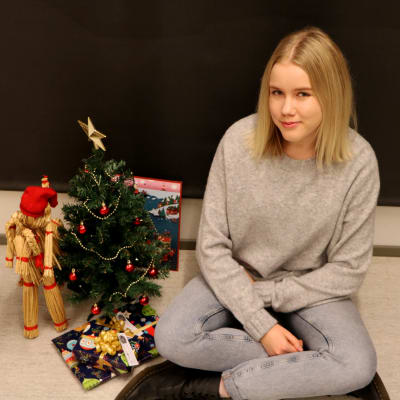 Anna sitter på golvet intill en julgran och annat julpynt.
