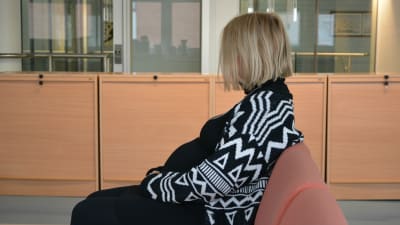 Gravid kvinna sitter vänd i profil mot kameran på en soffa