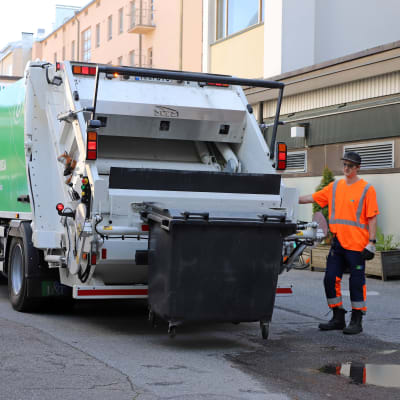 Jäteautonkuljettaja Tuure Vanhanen tyhjentää roskalaatikkoa jäteautoon Jyväskylässä, sähköpotkulauta auton vieressä.