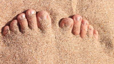 Fötter på sandstrand.