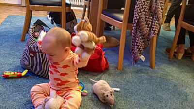 En baby sitter på gilvet och leker med godsedjur.