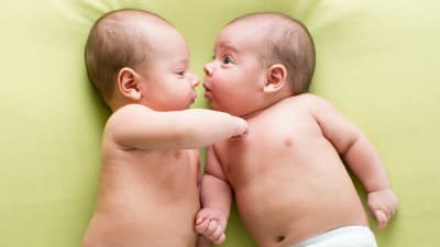 Två bebisar i blöjor ligger och tittar på varandra på en filt.