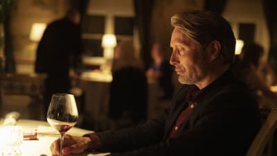 Närbild på Martin (Mads Mikkelsen) som sitter vid en bord med ett glas rödvin.