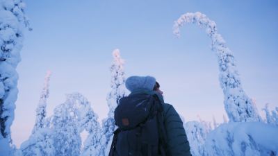 Nainen seisoo selin kameraan talvisessa ja lumisessa metsässä.