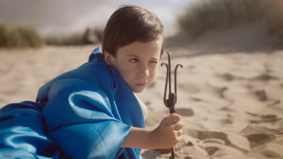Aatos ligger på stranden och leker Poseidon. Stillbild ur dokumentären Aatos ja Amine.