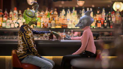 Två personer utklädda i masker är på en första dejt på en bar. Till vänster en man utklädd till en grön insekt och till höger en kvinna utklädd till en fisk..