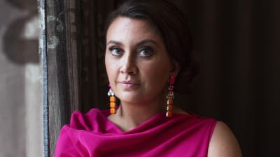 Camilla Läckberg vid ett fönster, iklädd mörkrosa skjorta. 