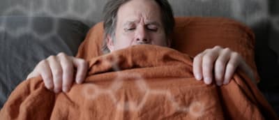 Patrik (Robin Svartström) makaa sängyssä raottaen peittoa ja katsoen alavartaloaan. 