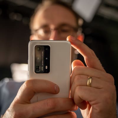 En man håller upp en mobiltelefon framför sig så att baksidan med kameran syns.