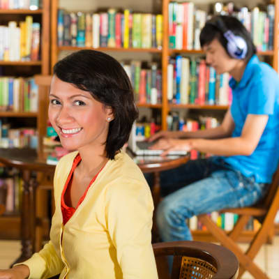 Flicka i gul skjorta sitter vid en dator i ett universitetsbibliotek.