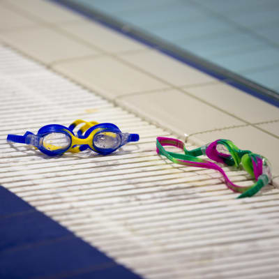 Färgglada simglasögon ligger på kanten till en bassäng i simhallen