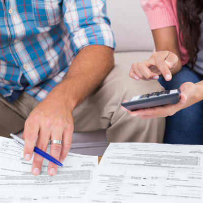 En man och en kvinna sitter och tittar på finanspapper med penna och miniräknare i hand.