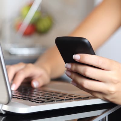 Kvinna som sitter framför en bärbar dator med en smarttelefon i handen.