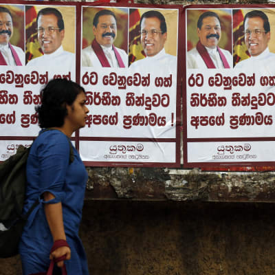En kvinna går förbi en vägg täckt av planscher på president Sirisena och nya premiärministern Rajapaksa 