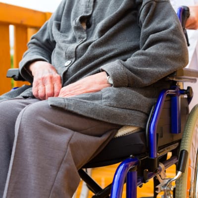 Äldre person sitter i en rullstol som en vårdare skuffar fram.