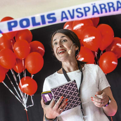 Författaren carina Nunstedt på en scen med röda ballonger i bakgrunden