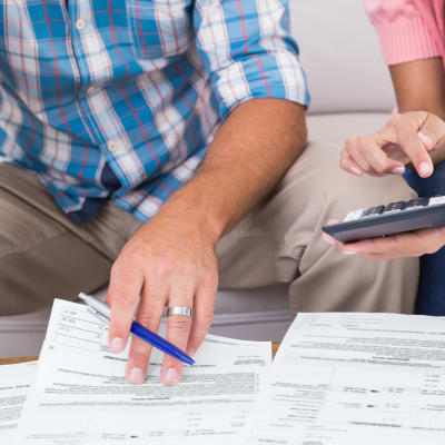En man och en kvinna sitter och tittar på finanspapper med penna och miniräknare i hand.