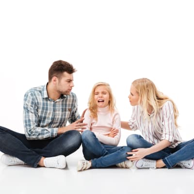 en mamma och pappa sitter på golvet och försöker diskutera med sin dotter som gråter