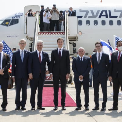 Bild på kostymklädda män poserar utanför ett vitt flygplan.