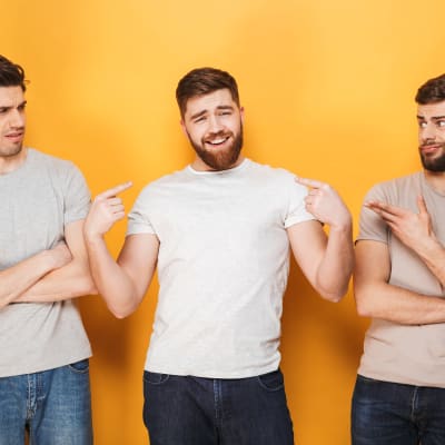 Tre unga män i ljus t-skjortor, den i mitten ler självsäkert medan de andra tittar surt på honom