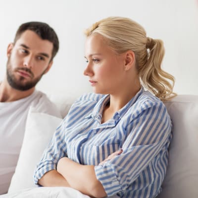  Mörkhårig man och blond kvinna sitter i soffa och ser sorgsna ut