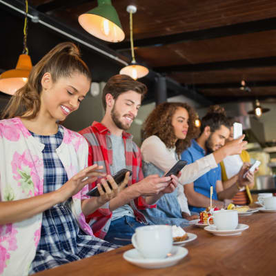 Femmunga människor sitter på ett café, alla sysslar med sina mobiltelefoner