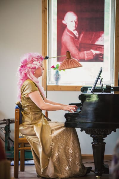 Pianisti Sonja Hendunen soittaa flyygeliä, päällä kullanvärinen iltapuku, päässä pinkki peruukki