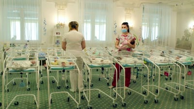 Två sköterskor står i ett rum fullt av nyfödda bebisar i genomskinliga sängar.
