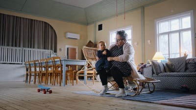 En kvinna sitter med sitt barnbarn i famnen i ett hem.