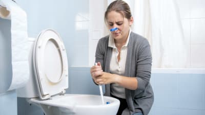 Kvinna med bykknipa på näsan skrubbar smutsig toalettstol. 