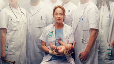 Chefsbarnmorskan Ella (Sofie Gråböl) håller en baby i famnen.