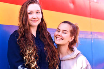 Två unga kvinnor sitter utaför en cirkusvagn och ler.
