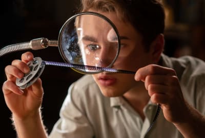 En ung man tittar på en filmremsa genom ett förstoringsglas.