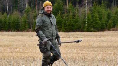 Heikki Räisänen går på en åker med en metalldetektor och letar efter metallföremål