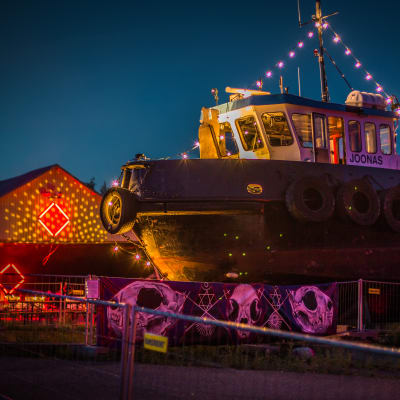 Upplyst båt och varvsbyggnad på H2Ö-festivalen.