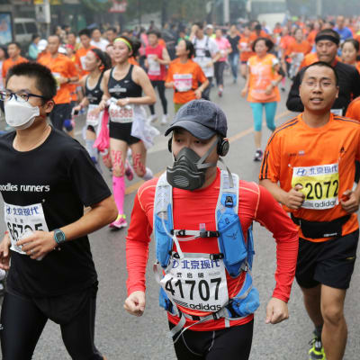 Kineser med andningsskydd springer maraton.