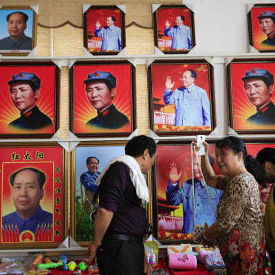 Besökare tittar på souvenirer framför en vägg med porträtt av Mao Zedong i Shaoshan i Hunanprovinsen i Kina. Shaoshan var Maos hemstad.