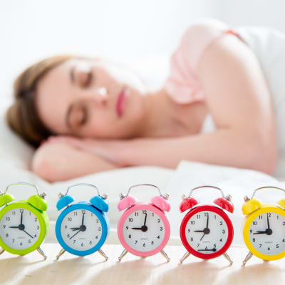 En kvinna som sover och har många väckarklockor bredvid sängen.