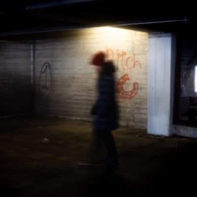 Nainen pimeähkössä autohallissa jonka seinässä lukee "Pitch".