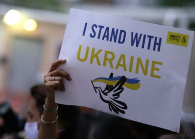 En hand håller upp ett plakat med amestys logo och en fredsduva där det står "I stand with Ukraine".