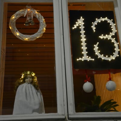 Ett husfönster med numret 13 och en docka med vit dräkt och luciakrona.