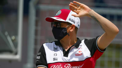Kimi Räikkönen med Alfa Romeo-tröja, keps och svart munskydd hälsar på publiken.