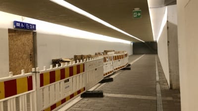 En tunnel med vita väggar och asfalterat golv. Tillfälliga staket till vänster.