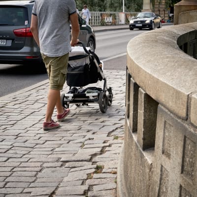 En pappa med barnvagn går längs en trottoar.