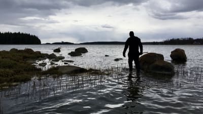En man går på vattnet bland stenar på en strand.