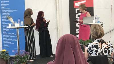 Två kvinnor i hijab intervjuas av en tredje kvinna på en mindre scen.