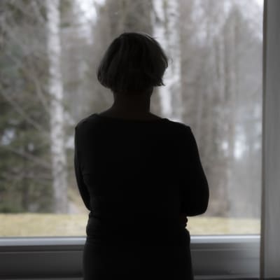 Tumma naisen hahmo katsoo ulos ikkunasta maisemaa.