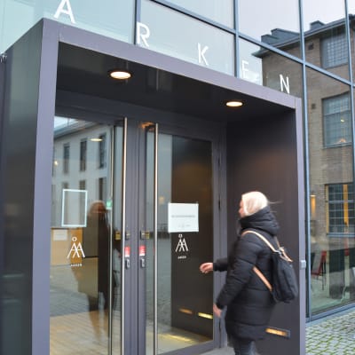 En kvinna med ljust hår sträcker sig mot en dörr in till Åbo Akademis hus Arken i Åbo.