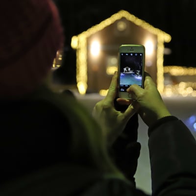Nainen ottaa kännykkäkuvaa Mikkelin Emolassa sijaitsevasta talosta, joka on koristeltu jouluvaloilla.