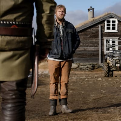 På bilden syns norska skådespelaren Tobias Santelmann som står framför ett trähus i fjällmiljö.